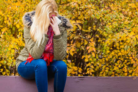 Sad woman sitting on bench in park during autumn weather hiding face in hand, feeling terrible depressed.の写真素材