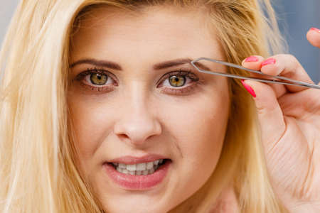 Woman plucking eyebrows depilating with tweezers closeup part of face. Girl tweezing removing her facial hairs..の写真素材