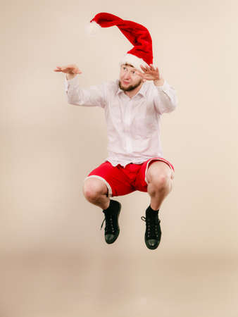 Active young man dancing and jumping in studio on beige. Handsome man in santa claus hat having fun. Christmas xmas season.の写真素材