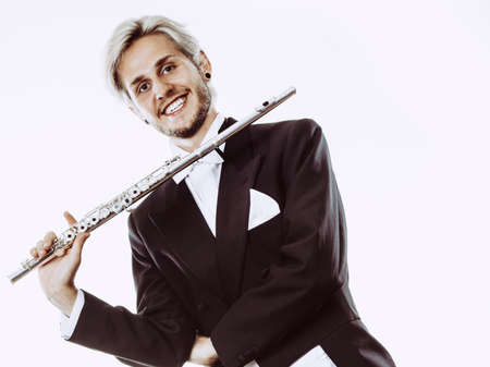 Classical music study concept. Male flutist musician performer playing flute. Young elegant man wearing tailcoat holds instrumentの写真素材