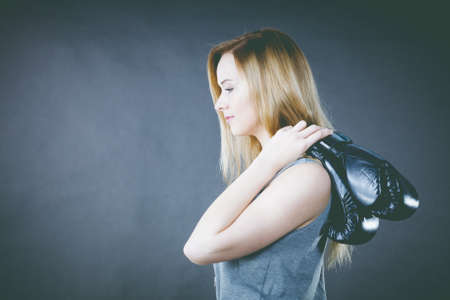 Sportsmanship fairplay and strong body. Blonde fit girl holding black punch gloves posing. Sport and fitness, power, exercising.の写真素材