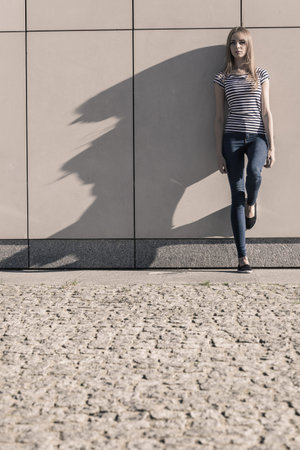 Young blonde woman in full length casual style against stone grunge wall
