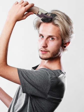 Hairdo hairstyle concept. Cool male hairstylist making self trendy haircut, fashion blonde metrosexual model going to shave his long hairの写真素材