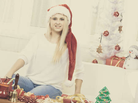 Seasonal concept. Blonde woman sitting on sofa, wearing santa hat, enjoying warm christmas atmosphere.の写真素材