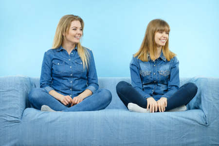 Friendship, human relations concept. Two happy women friends or sisters wearing jeans shirts sitting on sofa having fun.の写真素材