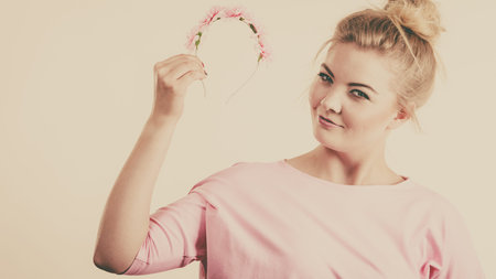 Happy positive cheerful smiling woman wearing pink dress with blonde hair holding flower wreath