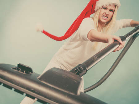 Woman vacuuming the house, last minute. Teen girl in santa helper hat with vacuum cleaner, angry furious face expression. Christmas time and housework concept.の写真素材