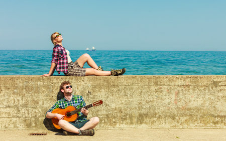 Young man playing guitar to his girlfriend outdoor by seaside - dating coupleの写真素材