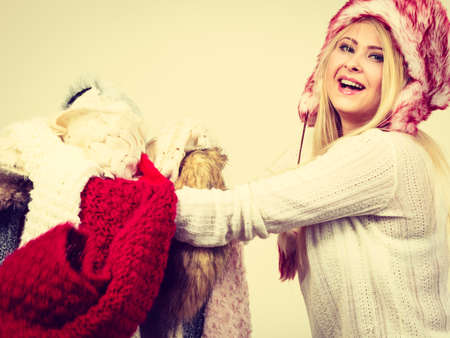 Accessories and clothing for cold days, fashion concept. Blonde woman in winter warm furry hat russian style holding big pile of clothes. Outfit picking problemの写真素材