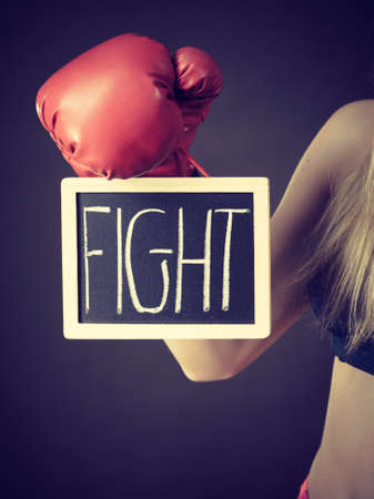 Young sporty woman wearing boxing glove holding black board with fight text sign. Studio shot on black background.の写真素材