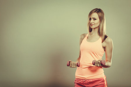 Bodybuilding. Strong fit woman exercising with dumbbells. Muscular blonde girl lifting weights...