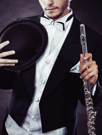 Classical music, passion, hobby concept. Elegantly dressed musician man holding flute and black fedora hat. Studio shot on dark backgroundの写真素材