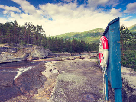 Beautiful view of norwegian mountain river in summer and sescue red lifebuoy life preserver saver ring on shoreの写真素材