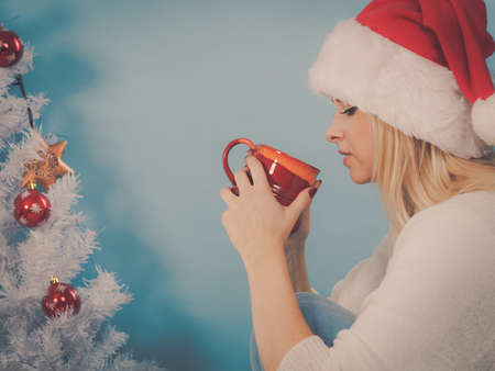 Relaxation during Christmas time concept. Woman in Santa hat holding holiday mug and drinking hot drink, coffee or tea enjoying her leisure time for relax.の写真素材