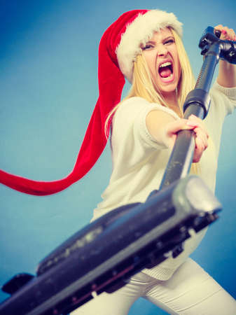 Woman vacuuming the house, last minute. Teen girl in santa helper hat with vacuum cleaner, angry furious face expression. Christmas time and housework concept.の写真素材