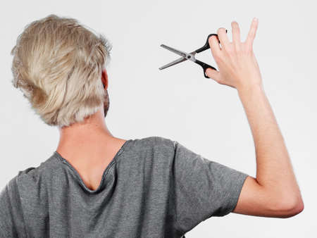 Coiffure hairstyle and haircut. Young cool guy holding special shears tool for work of hairdresser, rear viewの写真素材