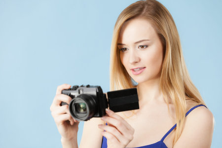 Photographer girl shooting images. Lovely blonde smiling woman with camera on blue background