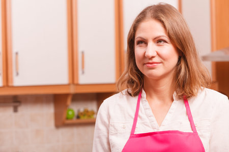 Vision and idea concept. Thinking wondering woman in kitchen. Contemplating housewife wearing pink apron at home.の写真素材