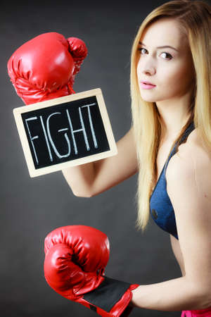 Young sporty woman wearing boxing glove holding black board with fight text sign. Studio shot on black background.の写真素材