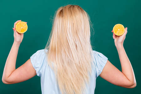 Healthy diet, haircare, refreshing food full of vitamins. Woman holding sweet delicious citrus fruit, lemon half showing her long blonde hair.の写真素材