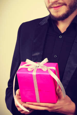 People celebrating xmas, love and happiness concept - cool young man holding present pink gift box in handの写真素材