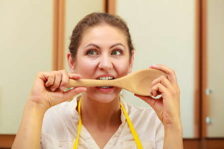 Cooking and preparing food meal concept. Thoughtful wondering and confused woman chef cook housewife holding biting ladle spoon in kitchen.の写真素材