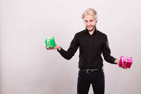 Celebration, special occasion, holidays concept. Trendy young man holding presents pink and green gift boxes in handsの写真素材