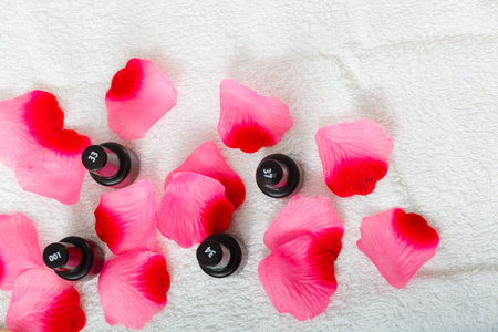 Black bottles with nail polish standing on white towel with roses petals, view from top.