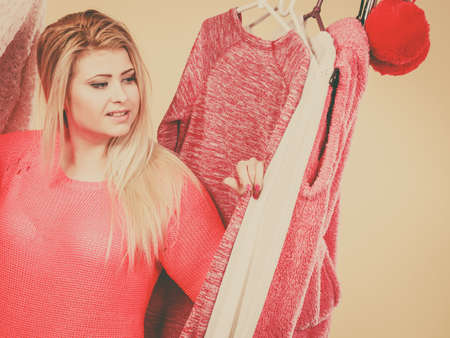 Fashionable style, trendy clothes, thinking about clothing concept. Blonde woman standing in wardrobe picking perfect winter outfit.の写真素材