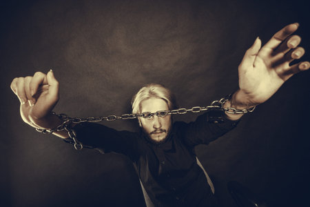 No freedom, social problems concept. Furious man with chained hands, studio shot on dark grunge...