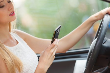 Distracted driver. Young attractive woman using mobile phone, texting or read message while driving...