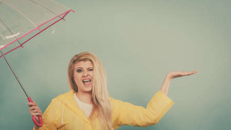Blonde woman wearing yellow raincoat holding transparent umbrella checking weather if it is raining.の写真素材