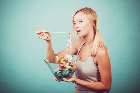 Diet, healthy food, weight loss and slim body concept. Fit fitness girl holding bowl eating colorful measuring tapesの写真素材