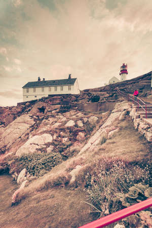 Tourist woman and historic red white lighthouse on the edge of rocky sea coast, South Norway, Lindesnes Fyr beaconの写真素材