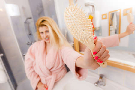 Happy blonde woman holding and showing her hair brush. Haircare and hairstyling concept.の写真素材