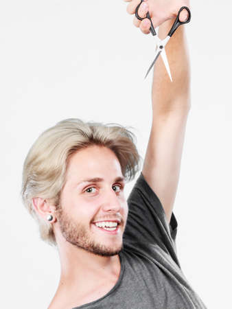 Hairstyle and haircut. Young cool guy barber holding shears tool ready to hair trimming. Blonde male with scissors creating new hairdo coiffureの写真素材