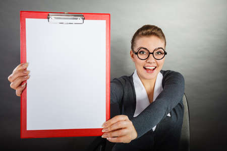 News and information in business work. Elegant blonde young woman with red empty clipboard and white piece of paper.の写真素材