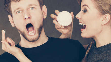 Protection and skincare. Stubborn girlfriend trying to apply cream on her boyfriend face. Man in uncomfortable situation with overprotective woman.の写真素材