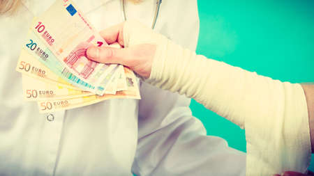 Corruption in healthcare industry. Female doctor bandaging male hand. Man giving money to woman. Bribery in medicine.の写真素材