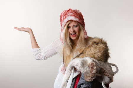 Accessories and clothing for cold days, fashion concept. Blonde woman in winter warm furry hat russian style holding big pile of clothesの写真素材