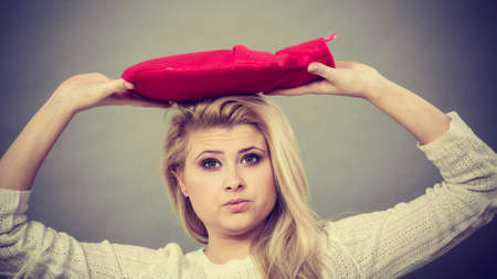Woman holding red hot water bottle on head to deal with headacheの写真素材
