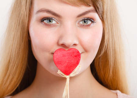Quietly about love and feelings. Lovely charming blonde female covering her mouth by little small heart on stick.の写真素材
