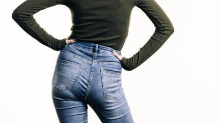 Unrecognizable woman standing backwards wearing slim fit blue jeans showing her buttocks curves.の写真素材