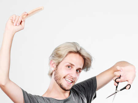 Style and fashion. Young trendy male hairstylist barber with new idea of look changing. Blonde guy with scissors and wooden comb creating hairdo coiffureの写真素材