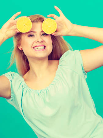 Woman smiling teen girl holding two halfs of yellow lemon citrus fruit in hands, on dark green. Healthy diet nutrition.の写真素材