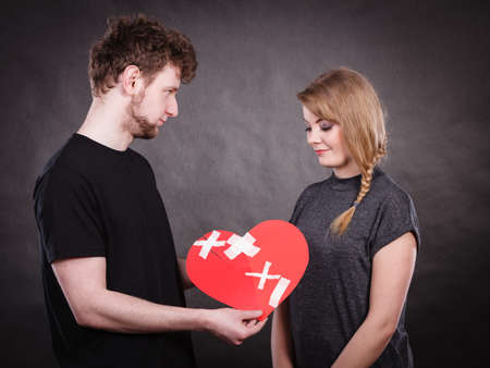Heal love concept. Couple woman and man holding two halves of broken heart fixed with plaster bandage going to be joined in one. の写真素材