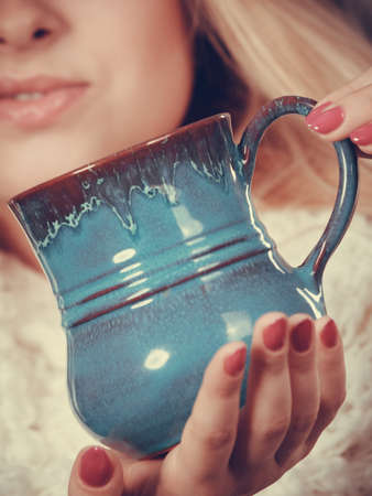 Accessories and clothes for cold days, fashion concept. Blonde woman in winter warm furry hat drinking hot drink from mug.の写真素材