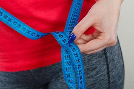 Diet, being fit and healthy concept. Woman hand measuring waist circumference with tapeの写真素材