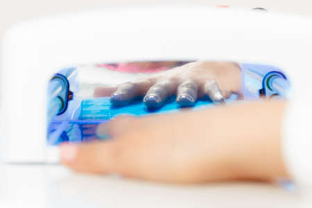Woman hand in uv led lamp drying gel hybrid manicure on nails. Beauty wellness spa treatment concept.の写真素材