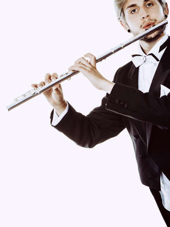Classical music study concept. Male flutist musician performer playing flute. Young elegant man wearing tailcoat holds instrumentの写真素材